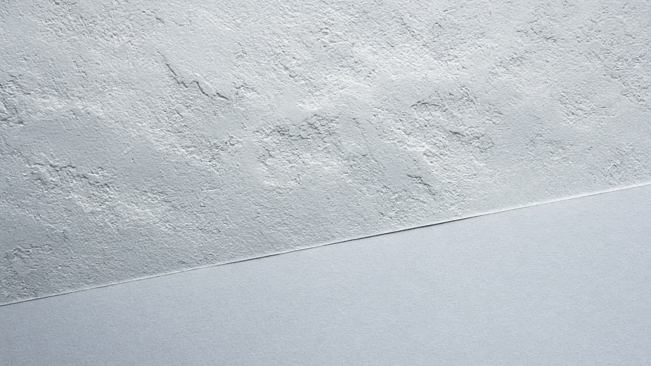 Raue, weiß gestrichene Putzfläche über glattem Papier